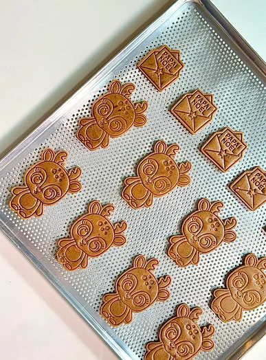 Assadeira com biscoitos de gingerbread em formato de rena e casinha, prontos pro forno