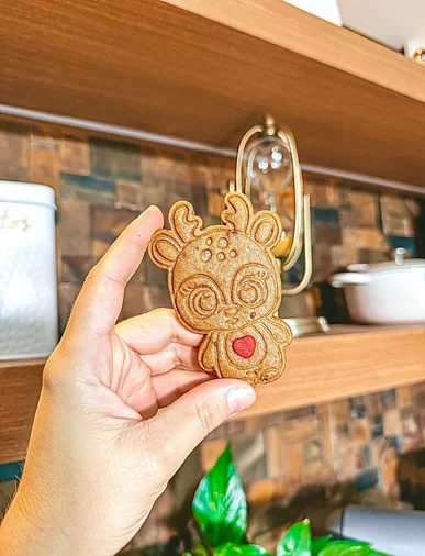 Mão segurando um biscoito de gingerbread em formato de rena, já assado
